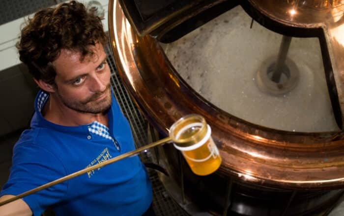 Braumeister mit Bierprobe vor Braukessel