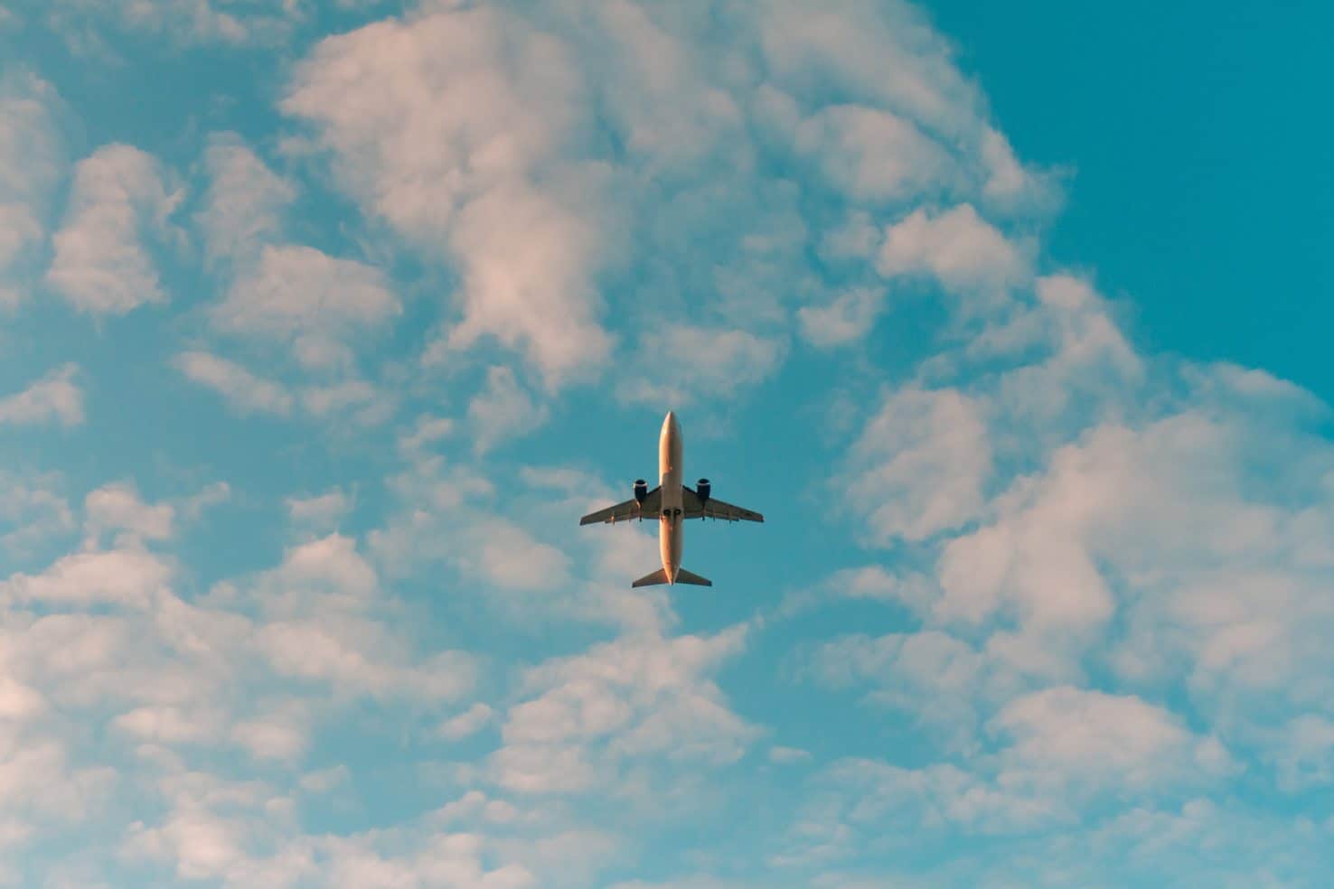 Unterseite eines Flugzeugs am blauen Himmel mit weißen Wolken