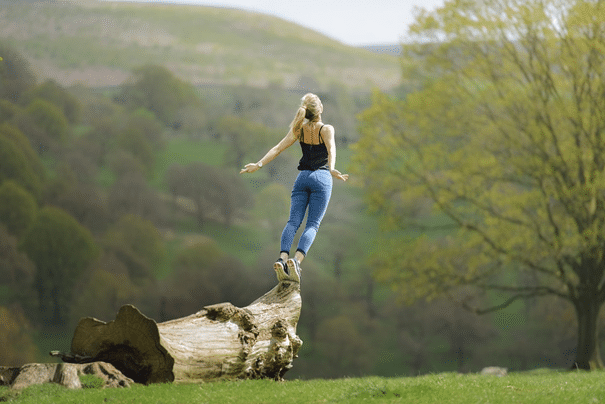 Frau steht auf Baumstamm wie auf einem Sprungbrett