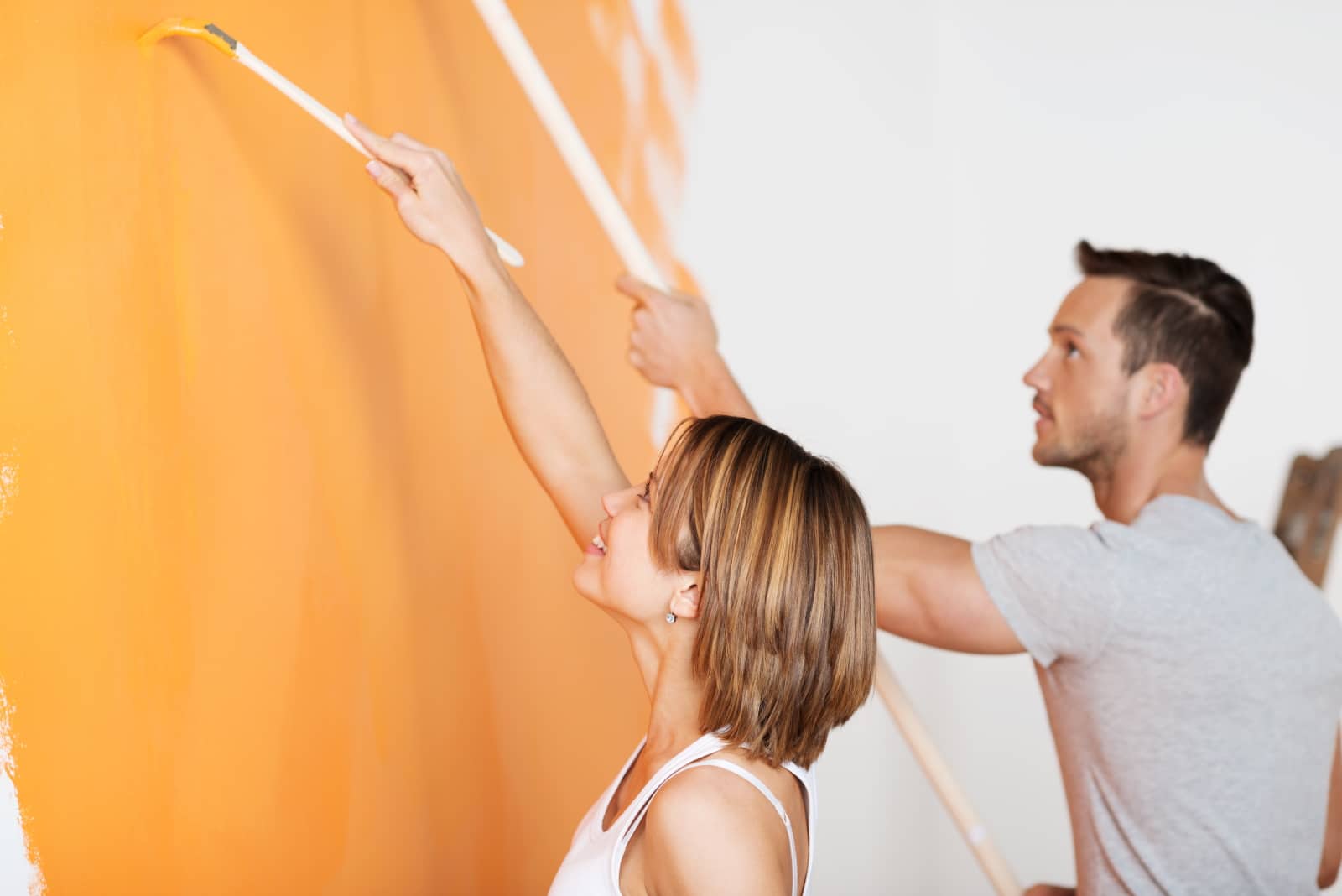 Junges Paar streicht eine weiße Wand mit Pinsel in der Farbe orange