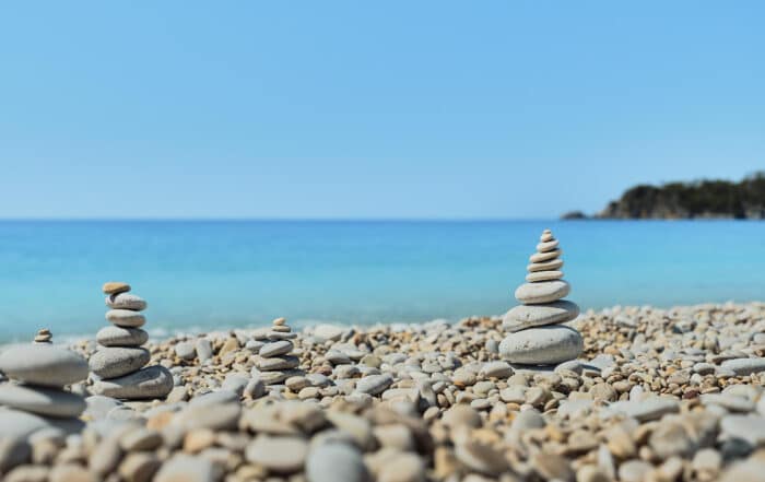 Steinkieselmännchen vor blauepyramiden am Kieselstrand vor blauem Meer