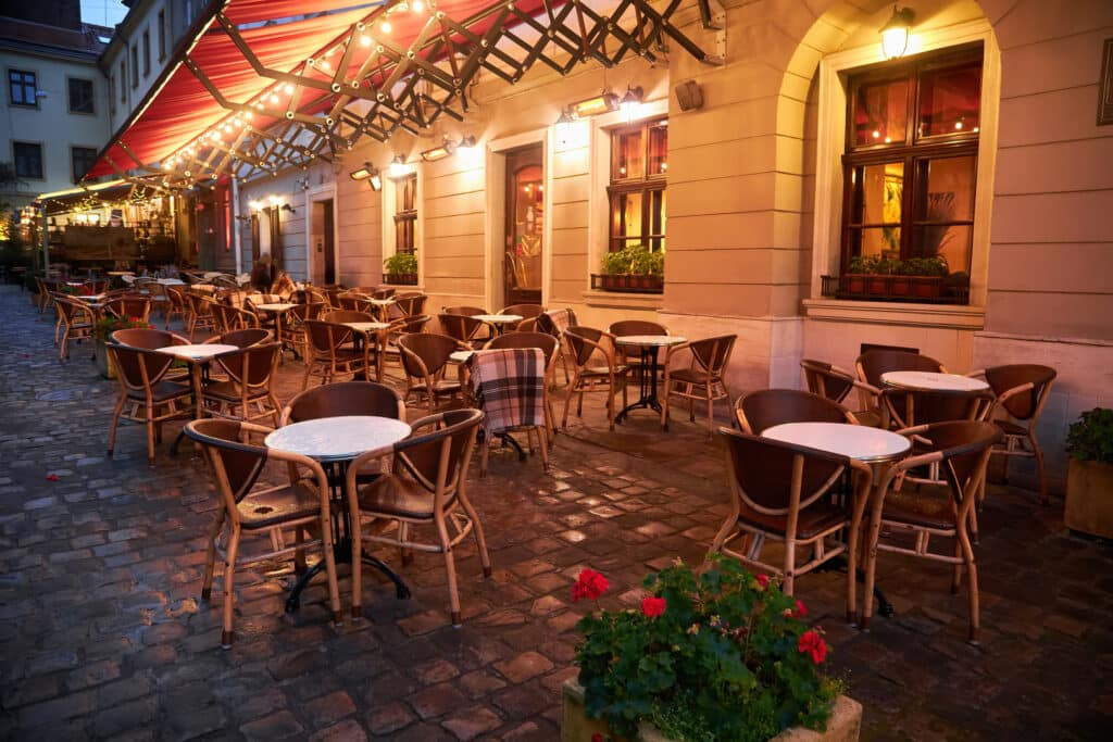 Beleuchtete Restaurantaußenbereich mit runden Tischen und Korbstühlen im Dämmerlicht
