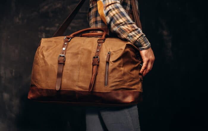 Hellbraune Weekender Reisetasche über der Schulter eines Mannes im karierten Hemd