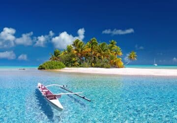 Kleine Insel mit Palmen auf weißem Sand und türkisfarbenen Wasser mit einem kleinen weißen Boot