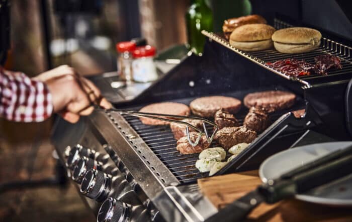 Grill bestückt mit Steaks und Burgern und Brötchen.