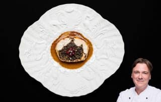 Ballotine vom Huhn auf weißen Porzellanteller mit breitem verziertem Rand mit abgerundeten Ecken.