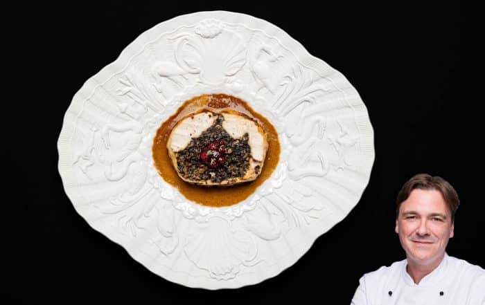 Ballotine vom Huhn auf weißen Porzellanteller mit breitem verziertem Rand mit abgerundeten Ecken.