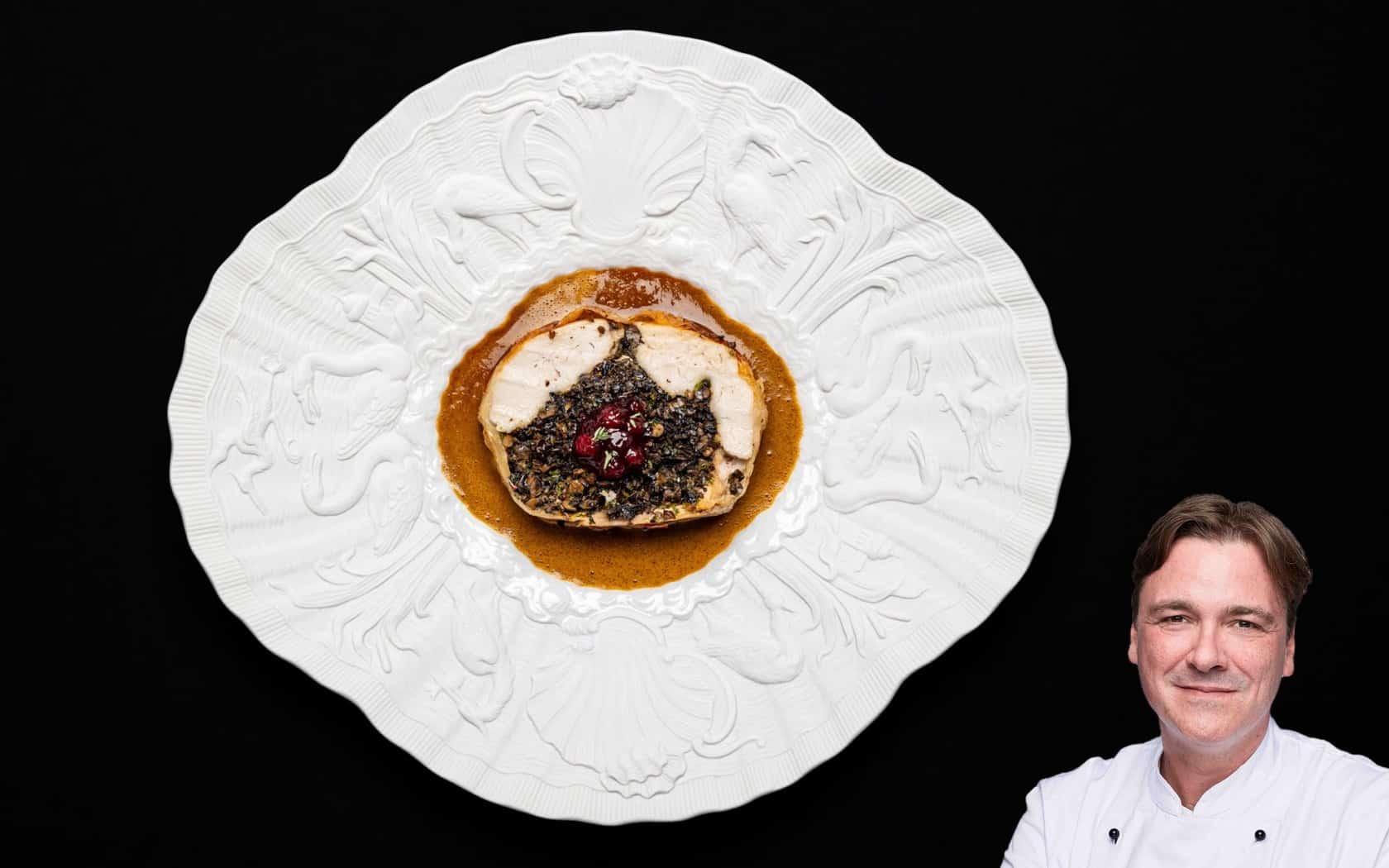 Ballotine vom Huhn auf weißen Porzellanteller mit breitem verziertem Rand mit abgerundeten Ecken.