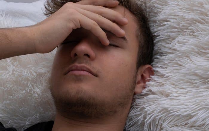 Detailansicht Kopf eines jungen Mannes mit geschlossenen Augen und Hand auf der Stirn