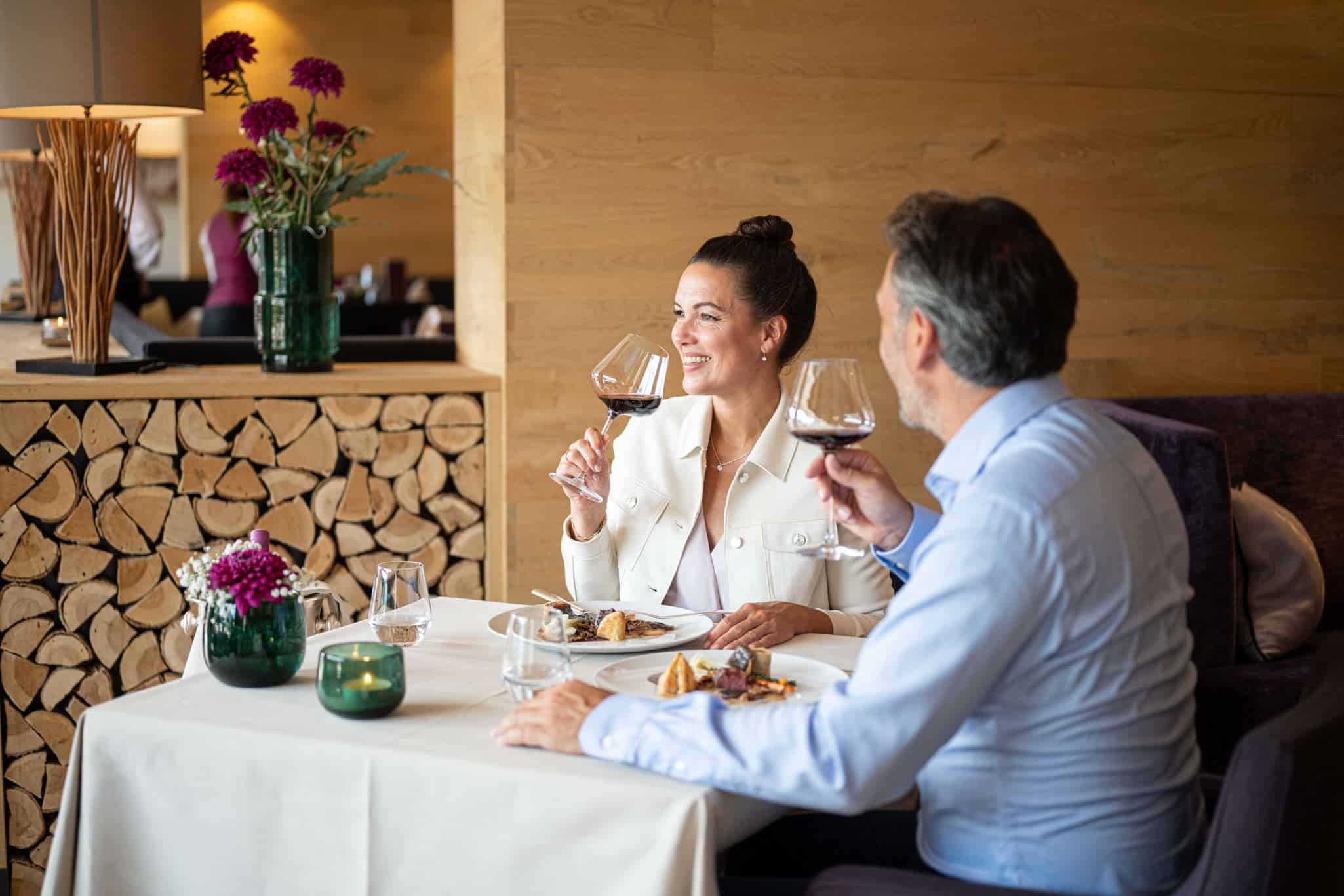 1_Exquisit Zwei Personen sitzen an einem gedeckten Tisch mit Essen und trinken Rotwein.