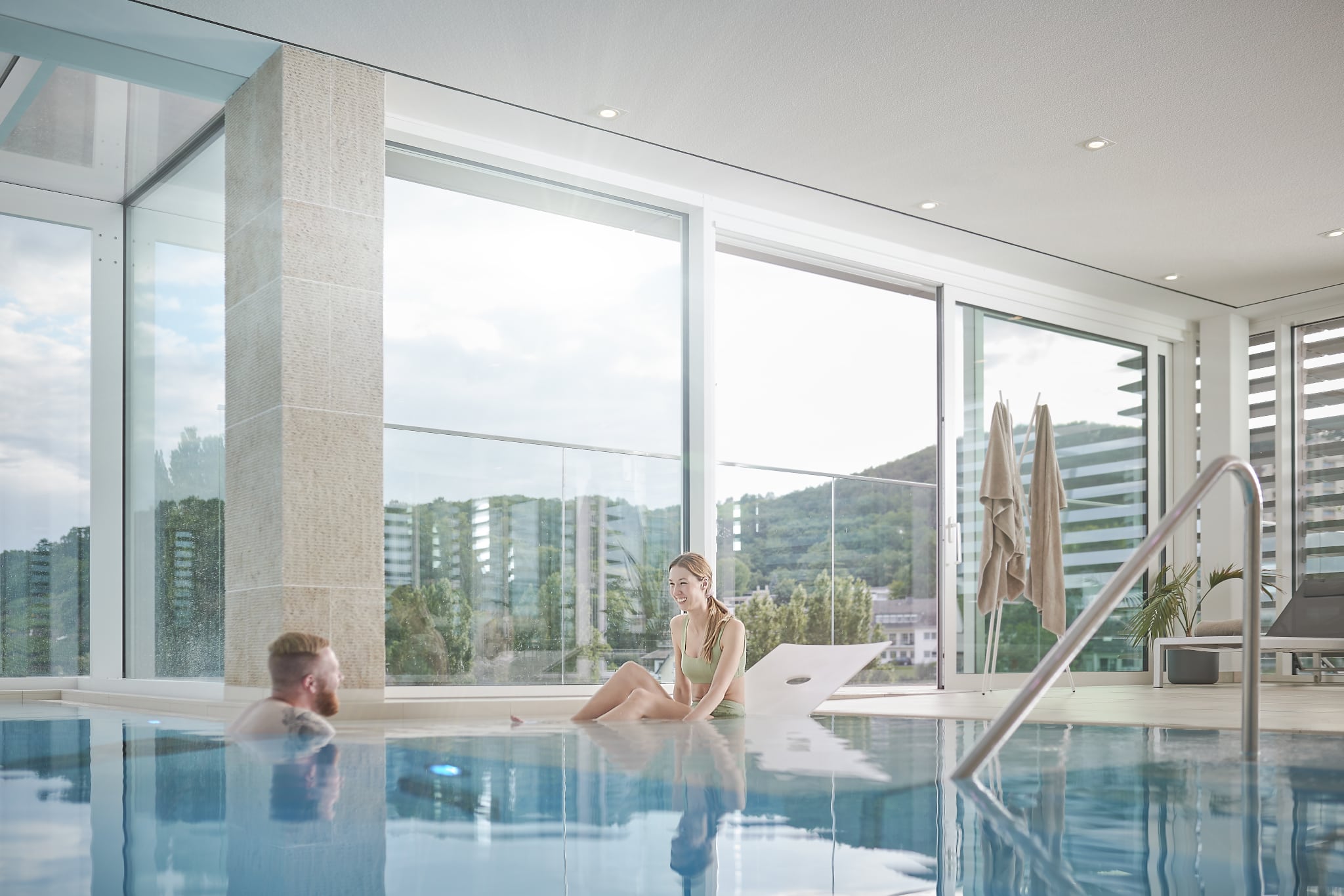 H16246mp_Premium_media_image_5 Innenpool mit großen Glasfronten, zwei Personen entspannen im Wasser.