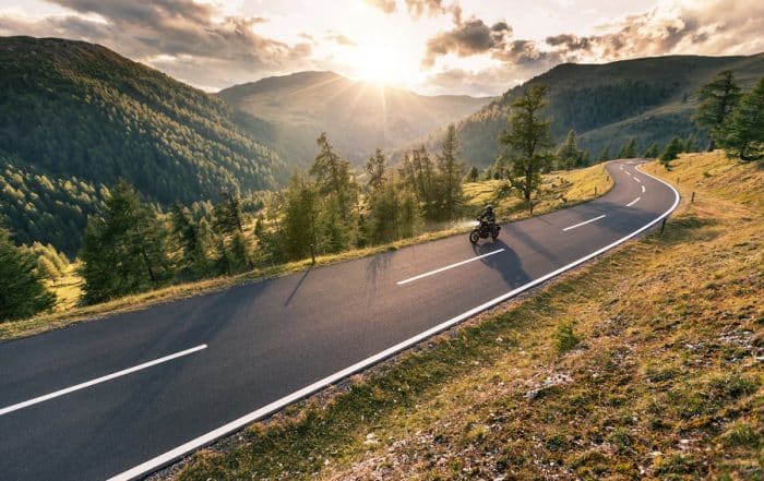 Motorradfahrer auf langer Straße in den Aplen.