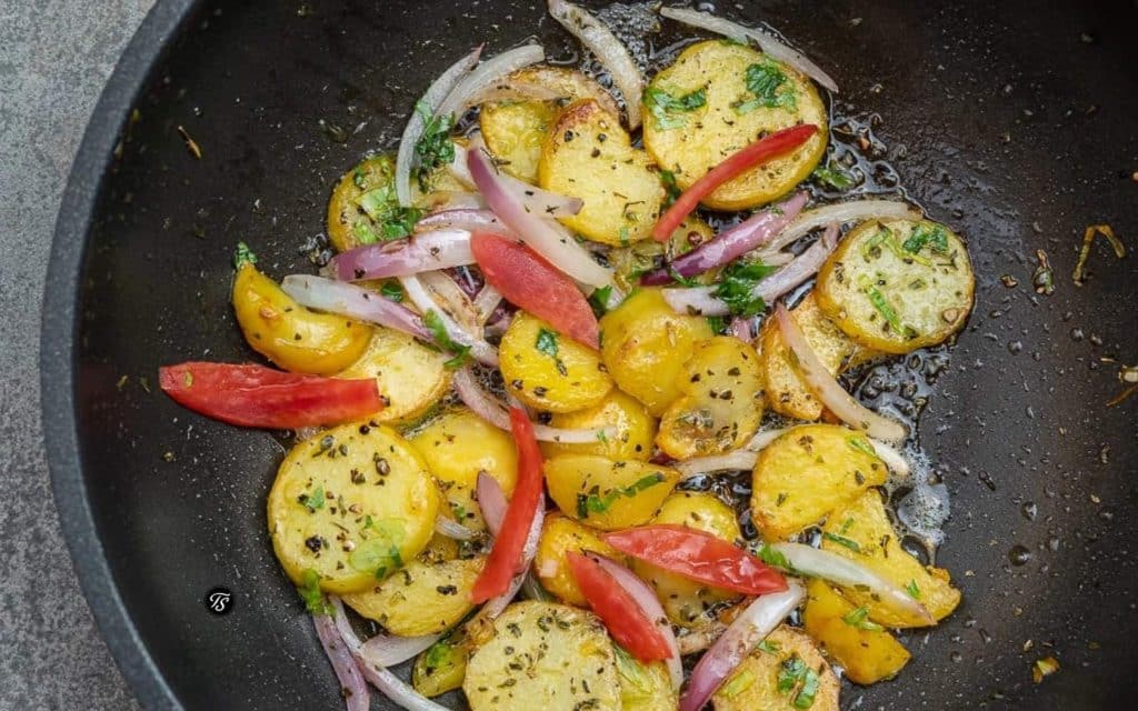 Bratkartoffeln mit roten Zwiebelspalten und Tomatenstreifen in dunkler Pfanne