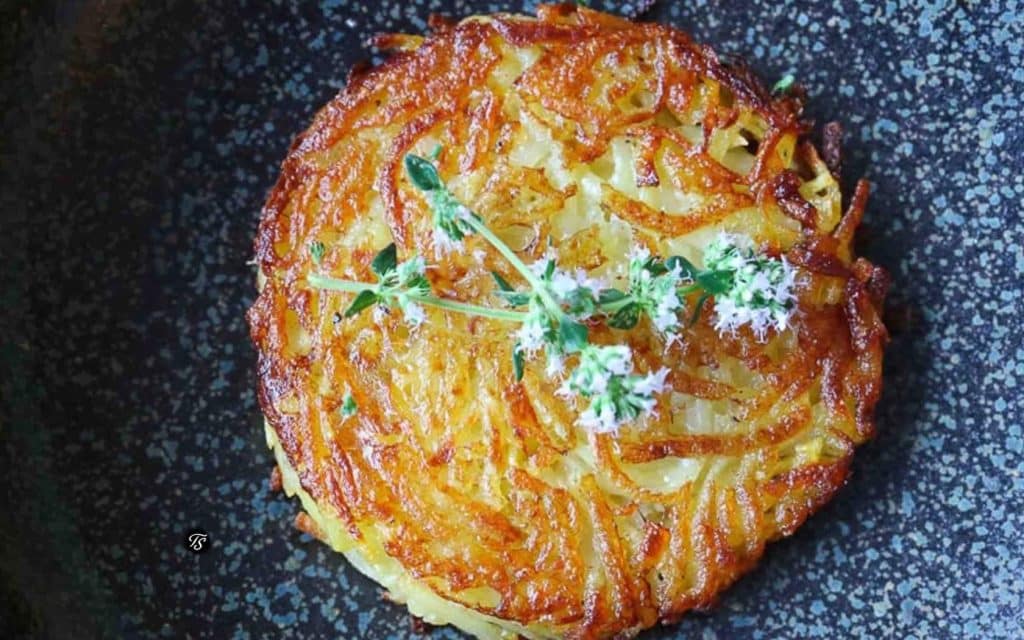 Kartoffelrösti in dunkler Pfanne mit Kräuterblüten dekoriert.