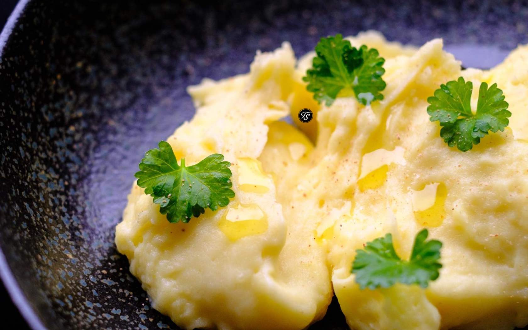 Kartoffelpüree in dunkler Schale mit Peterlienblättchen und zerlassener Butter