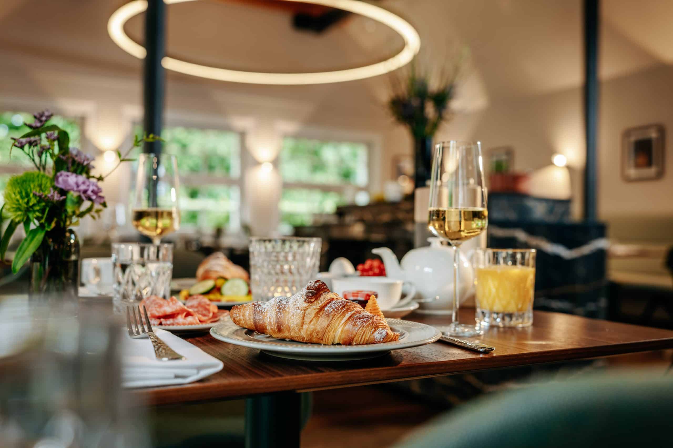 Frühstücksraum mit Nahaufnahme von Teller mit Croissant, Osaft und Sektglas auf einem Tisch