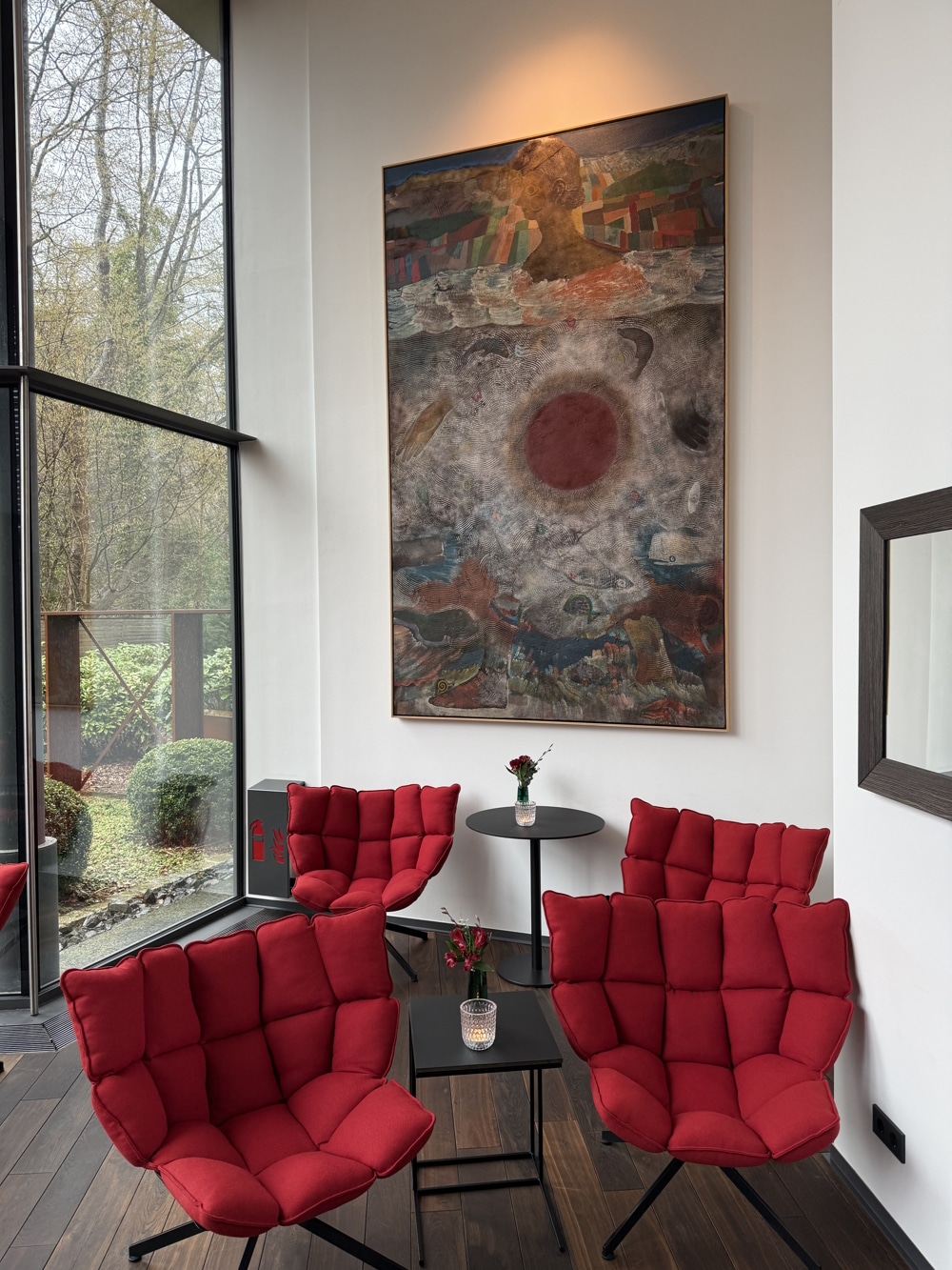 Lobby mit roten Designersesseln vor großen Bild und bodentiefer Fensterfront