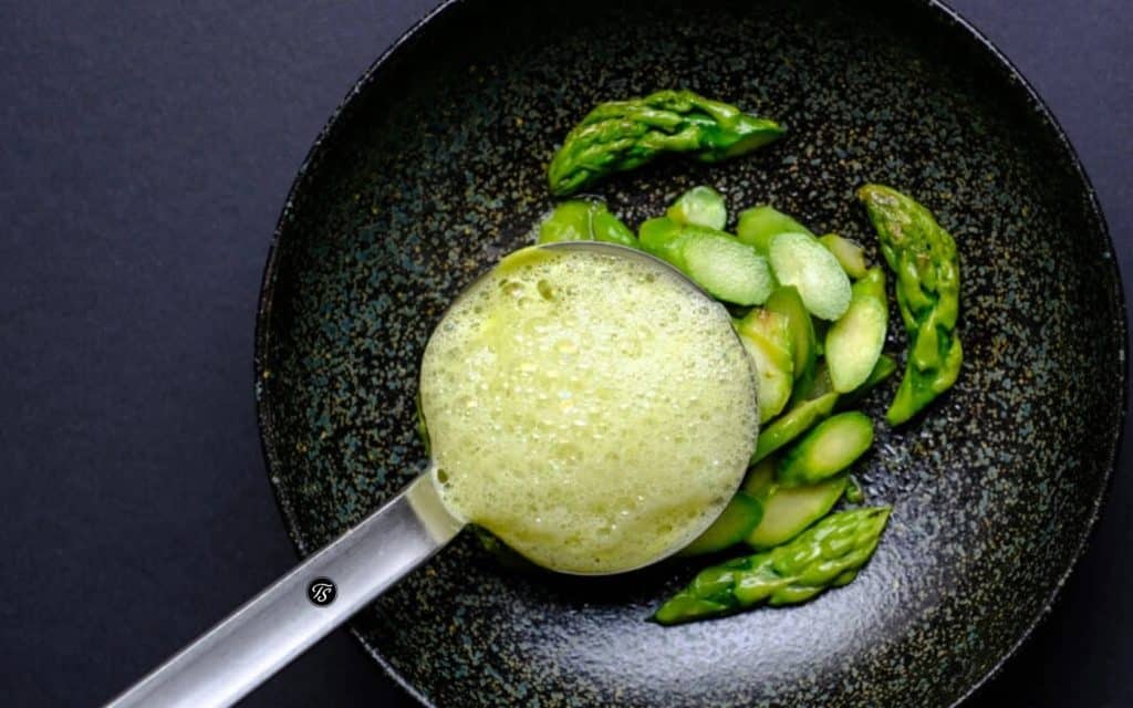 gruene-spargelsuppe-thomas-sixt-fuer-varta Grüner Spargel in dunkler Schüssel und Shöpfkelle mit Spargelsuppe