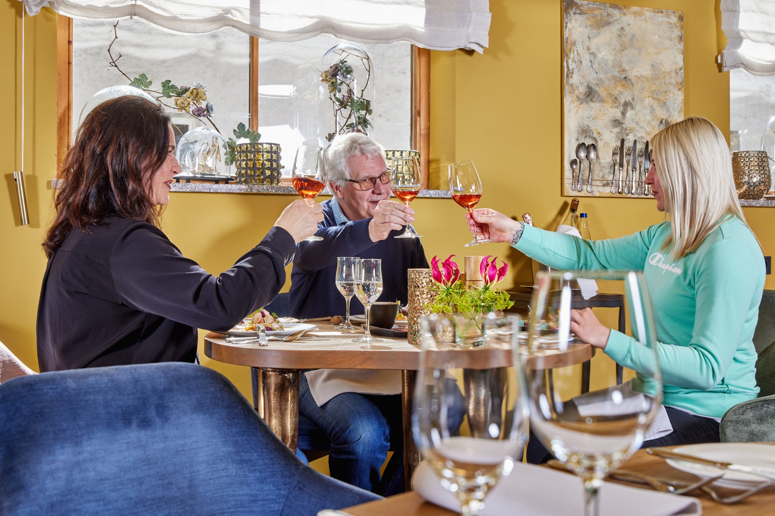 Gemeinsames Essen im 4Eck Restaurant Mehrere Gäste sitzen an einem Tisch im Restaurant und stoßen mit Getränken an, während sie gemeinsam essen.