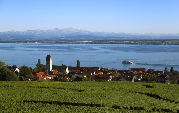 Blick über grüne Weinreben auf Hagnau un den Bodensee,mit Fährschiff im Hintergrund sieht man die Alpen