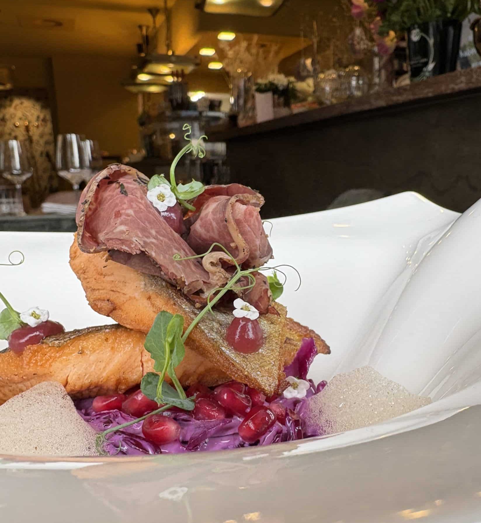 Kreative Küche im 4Eck Restaurant Ein kunstvoll angerichtetes Gericht mit Fleisch, Fisch und Garnitur steht auf einem Teller im Restaurant
