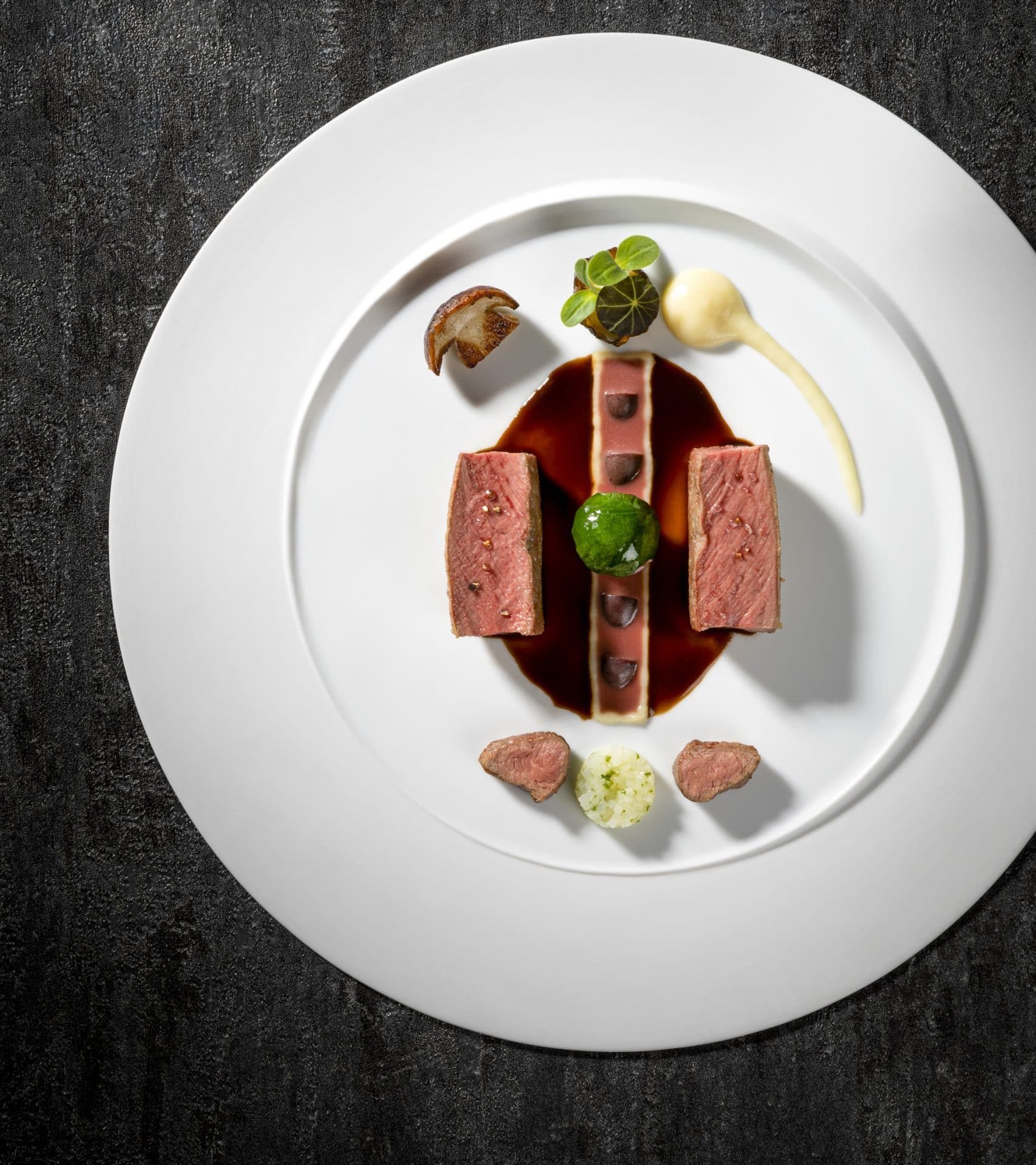 Elegantes Fine-Dining-Gericht mit rosa gebratenem Rehrücken, Jus und kunstvoll arrangierten Beilagen Modern interpretierter Rehrücken, präzise angerichtet mit feinen Komponenten und Jus.