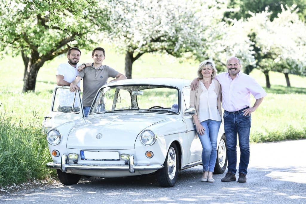 Familie Steinhauser – c KNIPPING Familie Steinhauser mit weißem VW Oldtimer im Frühling vor blühenden Ostbbäumen