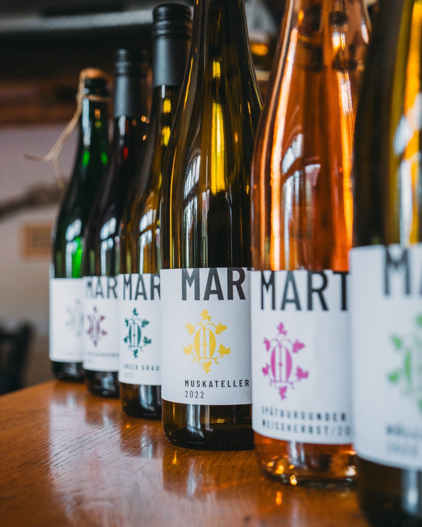 Weine Weingut Marte_1. Shooting_InstarMarketing_57sc Weinflaschen des Weinguts Marte mit unterschiedlich farbigem Logo auf einem Tisch von der Seite fotografiert