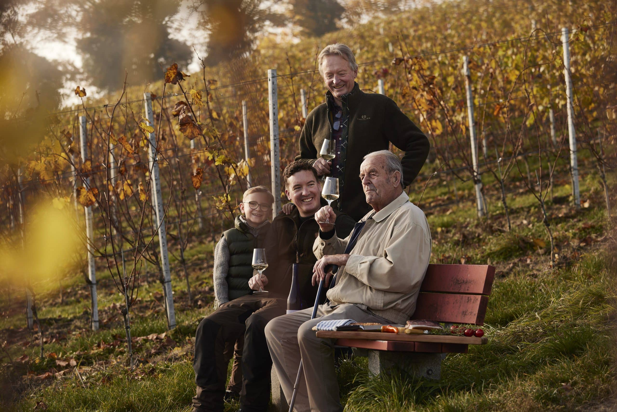4 Generationen Väter und Söhne der Familie Kress im Herbst auf einer Bank im Weinberg mit Weinglas