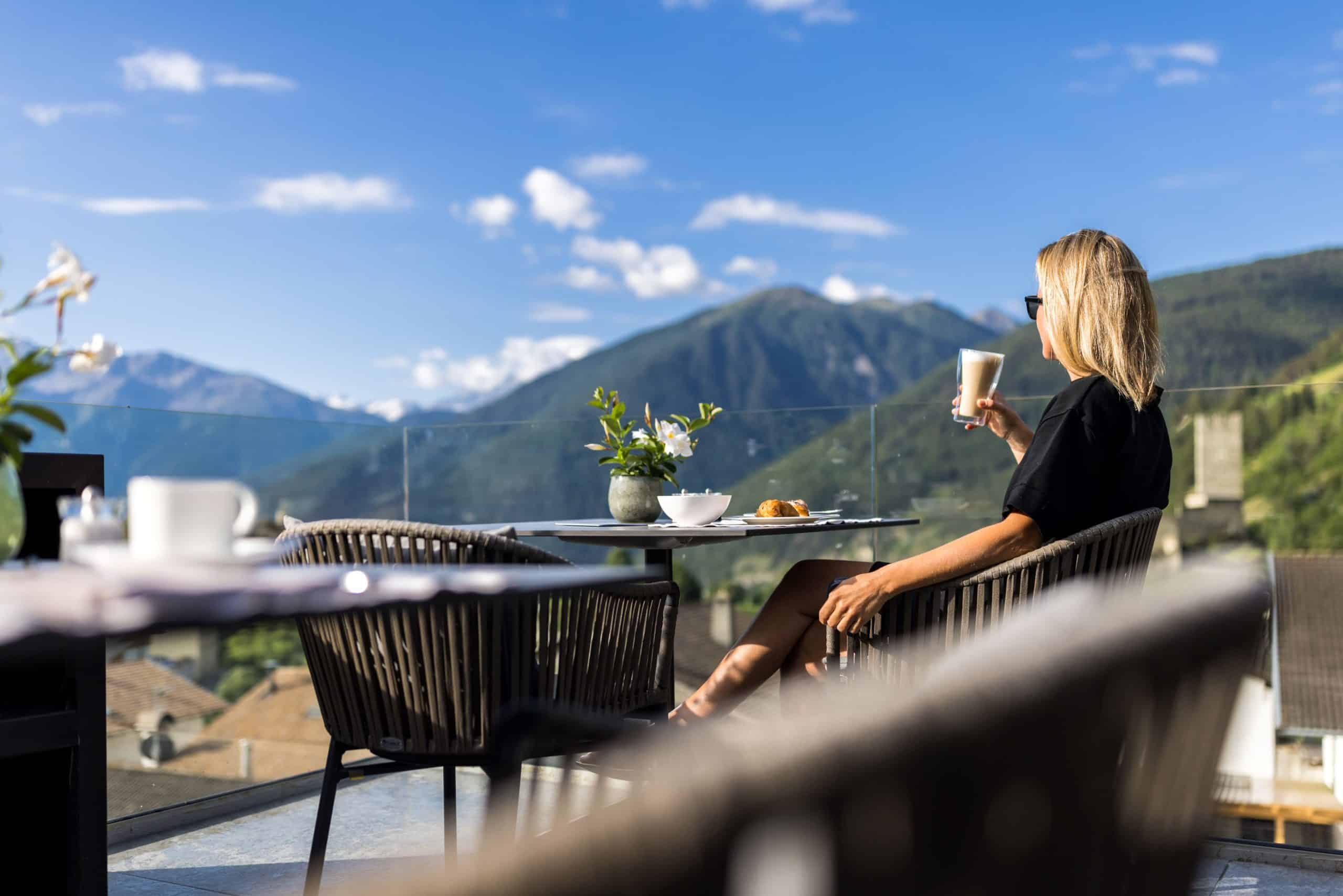 Frau sitzt auf der Terrasse und genießt das Bergpanorama