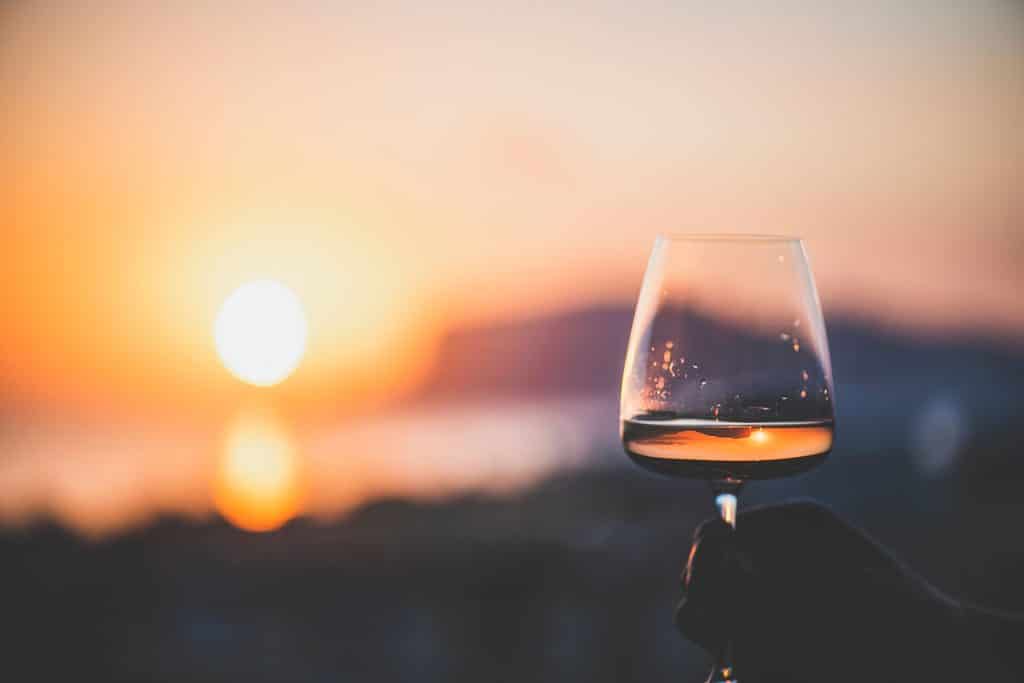 Man’s hand holding glass of wine with sea at background Man's hand holding glass of wine with sea at background