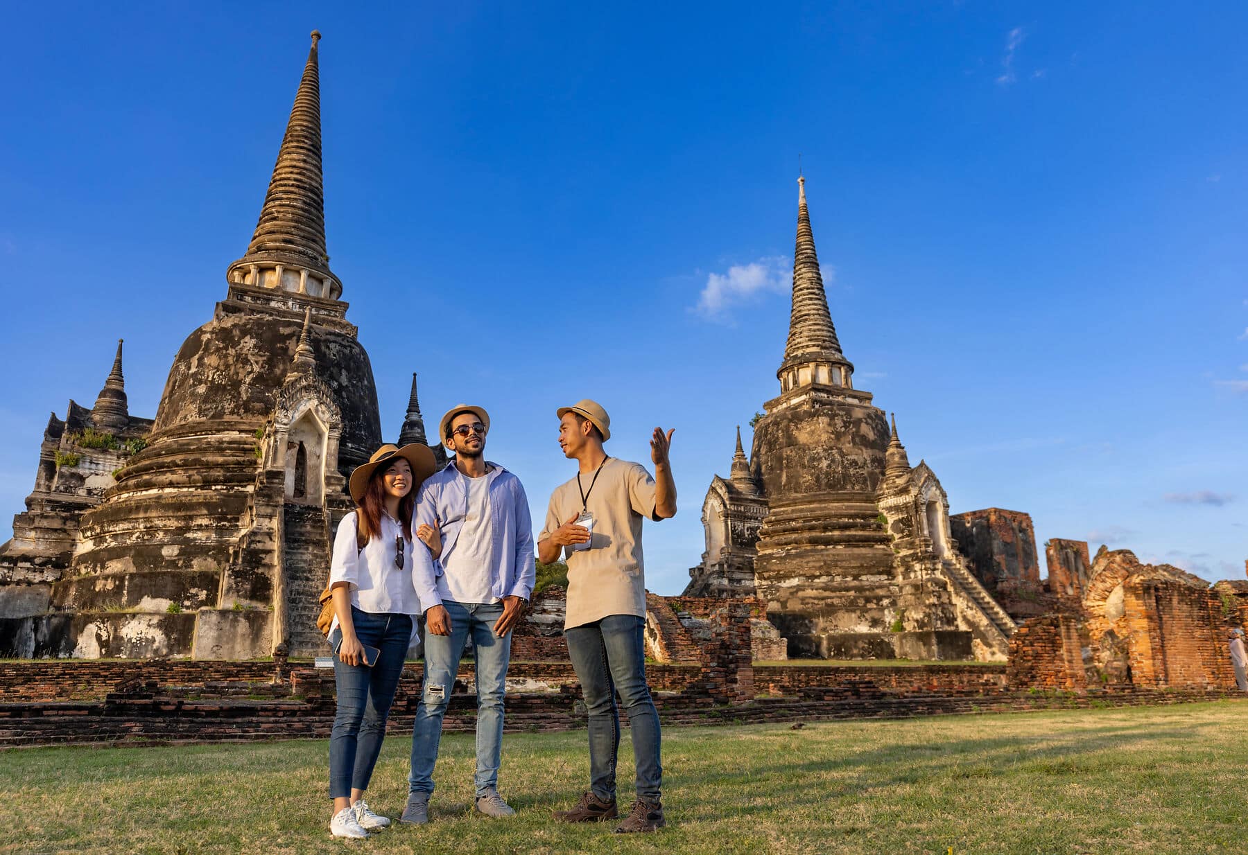 Thai local tour guide is explaining history of old Siam to the couple of tourist on their backpacker honeymoon travel to ancient temple of Ayutthaya, Thailand