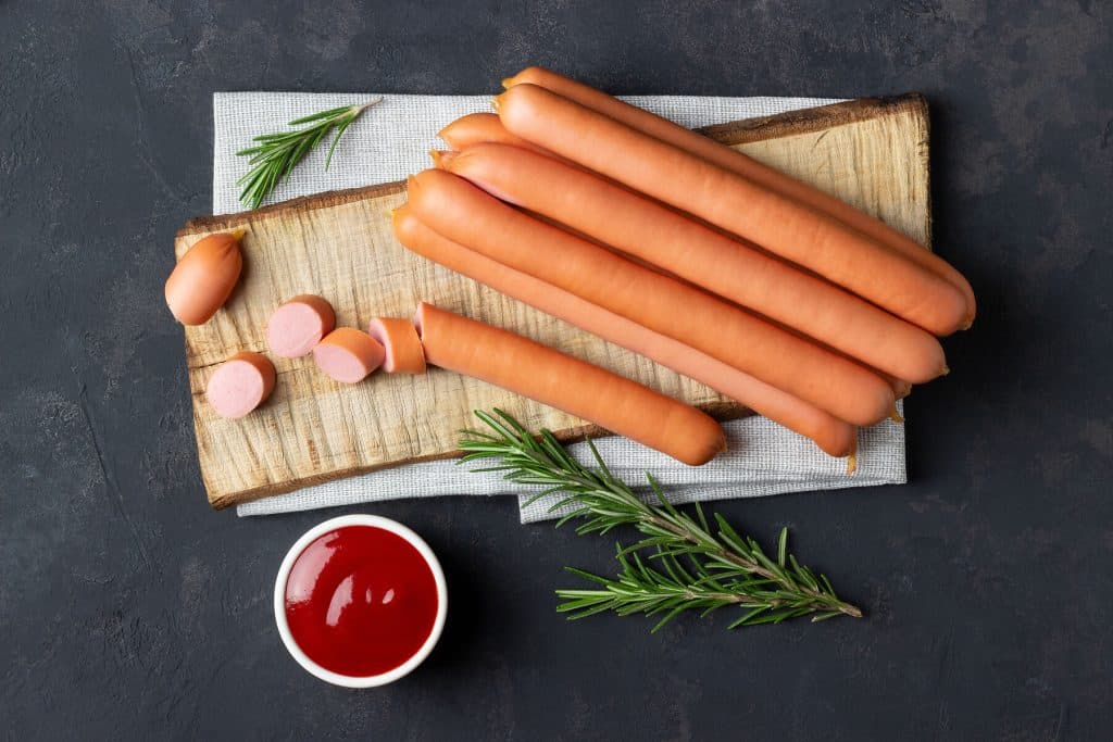 Raw frankfurter sausages Frankfurter Würstchen auf einem Schneidebrett aus Holz mit Rosmarinzweig und einem Schälchen mit Ketschup