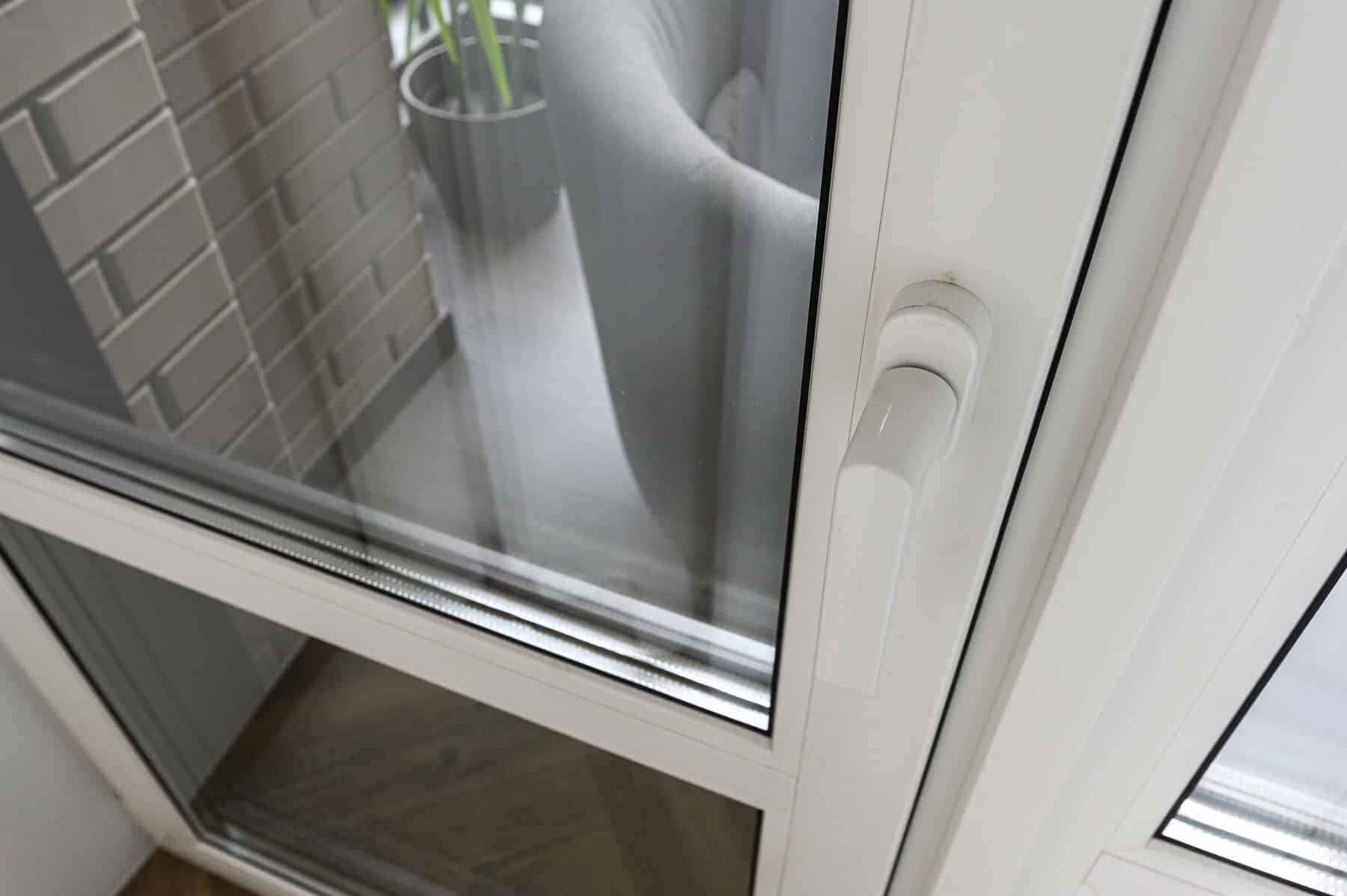 Kunstoffenster mit Doppelverglasung White PVC window frame, double-glazed pane, ergonomic white handle, clean profile lines, subtle shadow, neutral tones, textured brick wall, gray planter, green foliage, modern glazing