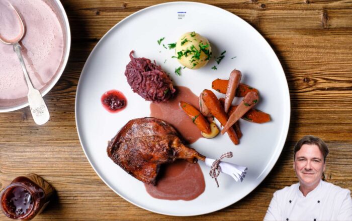 Titelfoto für Foodblogbeitrag von Thomas Sixt mit Rezept für Rotkohl mit weißem Telller auf Holztisch. Auf dem Teller ist Rotokohl mit Entenschlegel angerichtet, rechts unten ist das Portraitfoto von Thomas Sixt