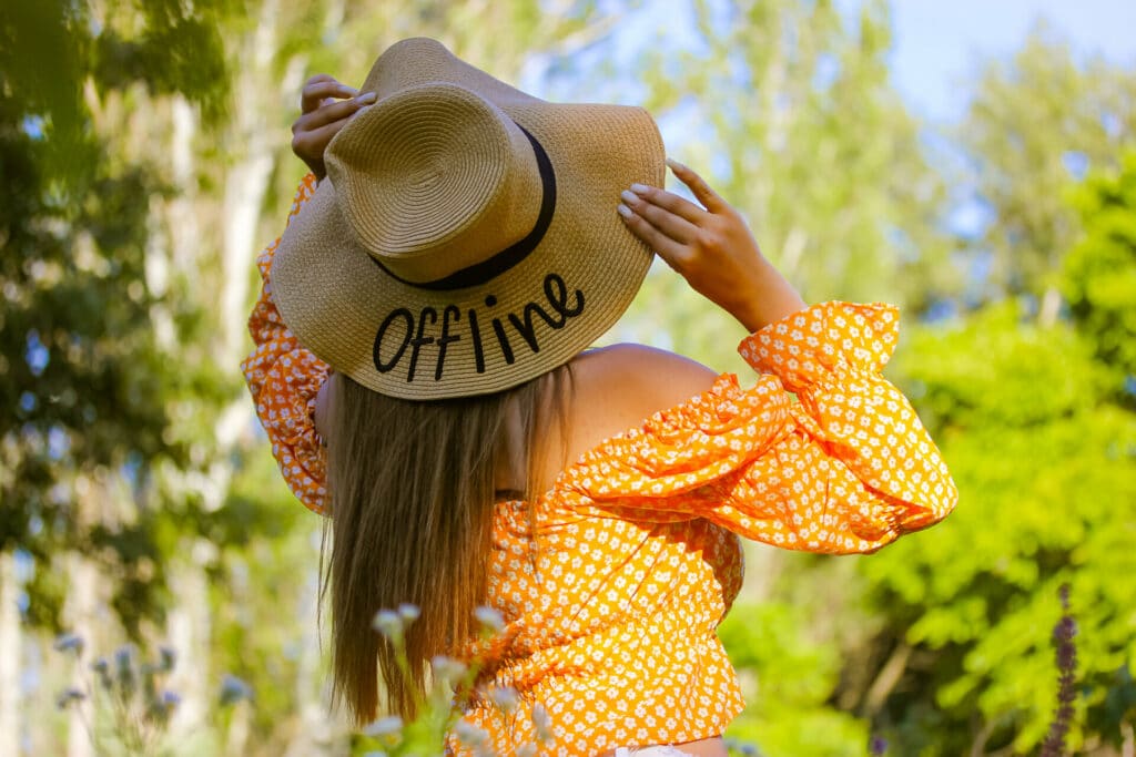 Junge Frau im Sommer mit Strohhut der die Aufschrift "offline" trägt