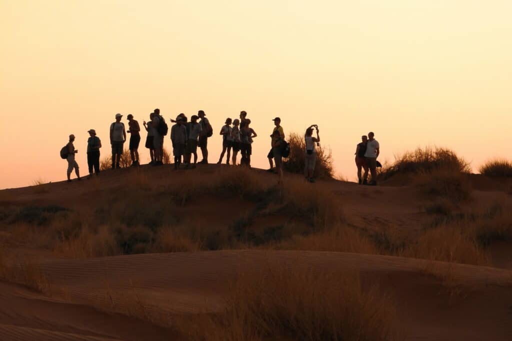 Eine Gruppe von Touristen stehen in einer Dünenlandschaft im goldenen Abendlicht.