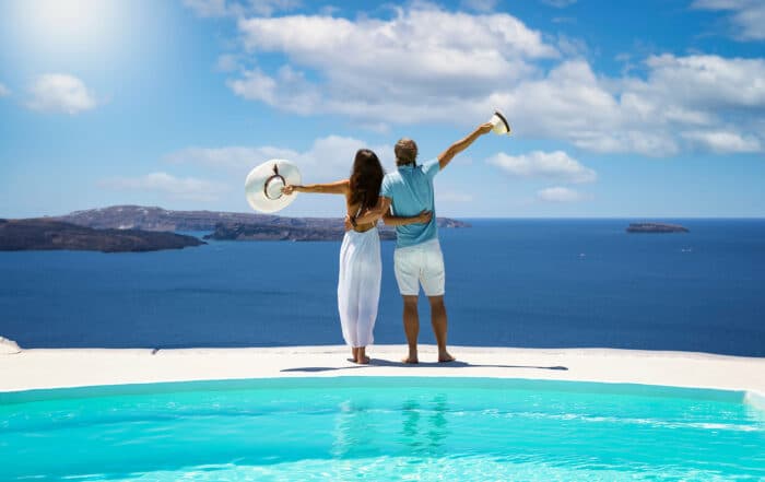 Ein Mann und eine Frau halten sich und stehen vor einem Panoramapool und blicken aufs Meer.