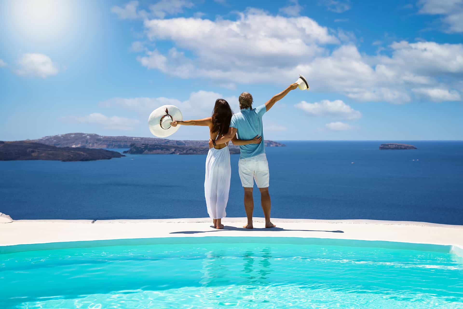 Ein Mann und eine Frau halten sich und stehen vor einem Panoramapool und blicken aufs Meer.