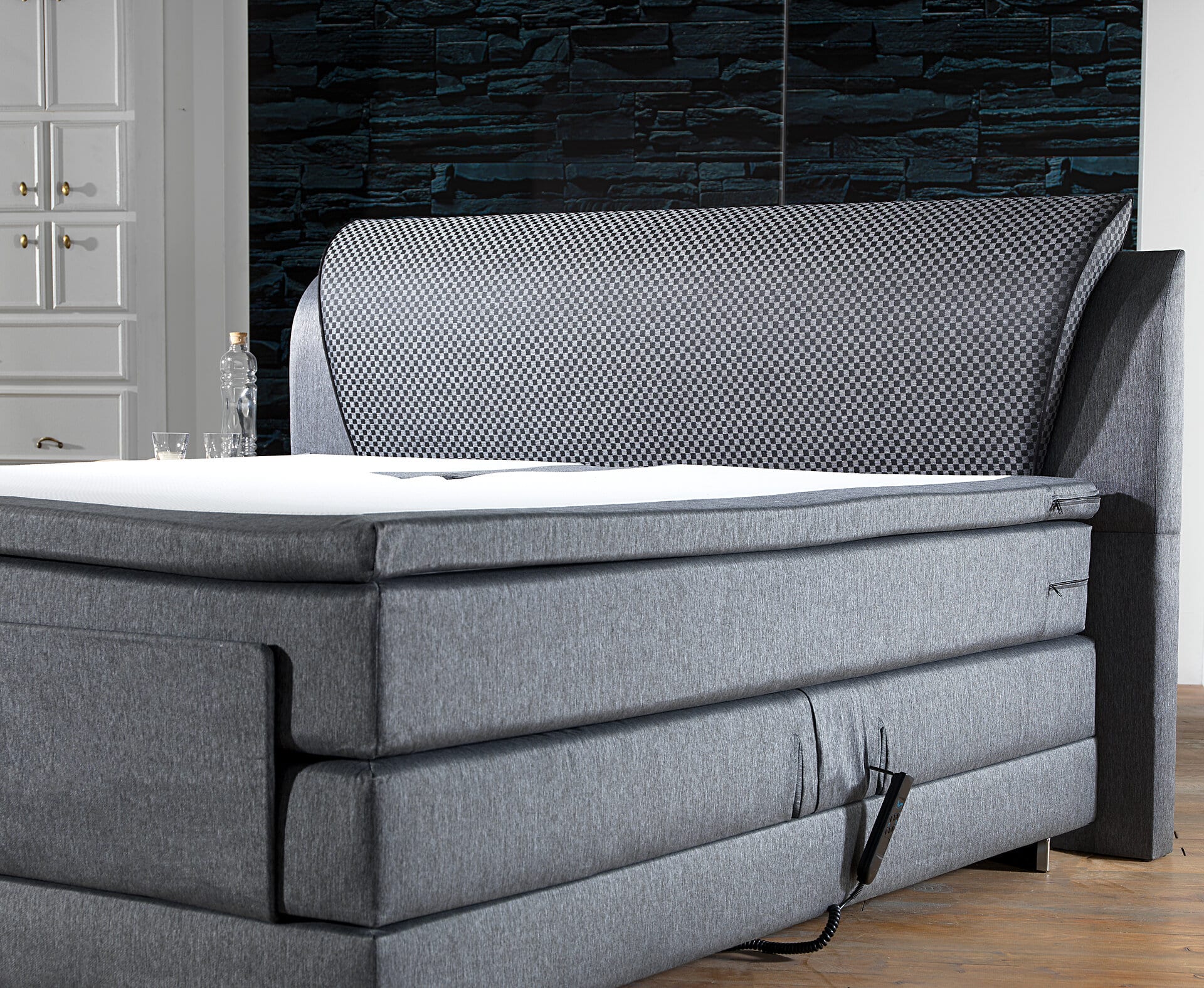 Graues Boxspringbett mit Bedienelement für die Höhenverstellung mit grau gemusterten Kopfende