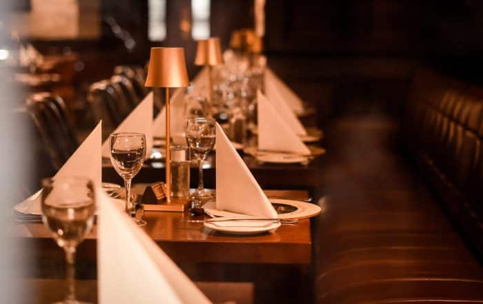 Restaurant im Bistrostil mit Tischen aus dunklem Holz und Lederbank, Tische sind eingedeckt mit Stehlampen auf jedem Tisch