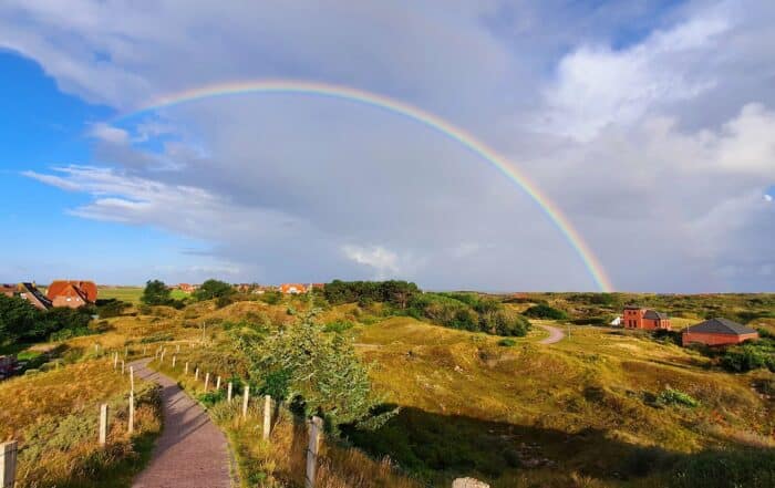 Blick über die Dünen mit Häusern unter einem Regenbogen auf Baltrum
