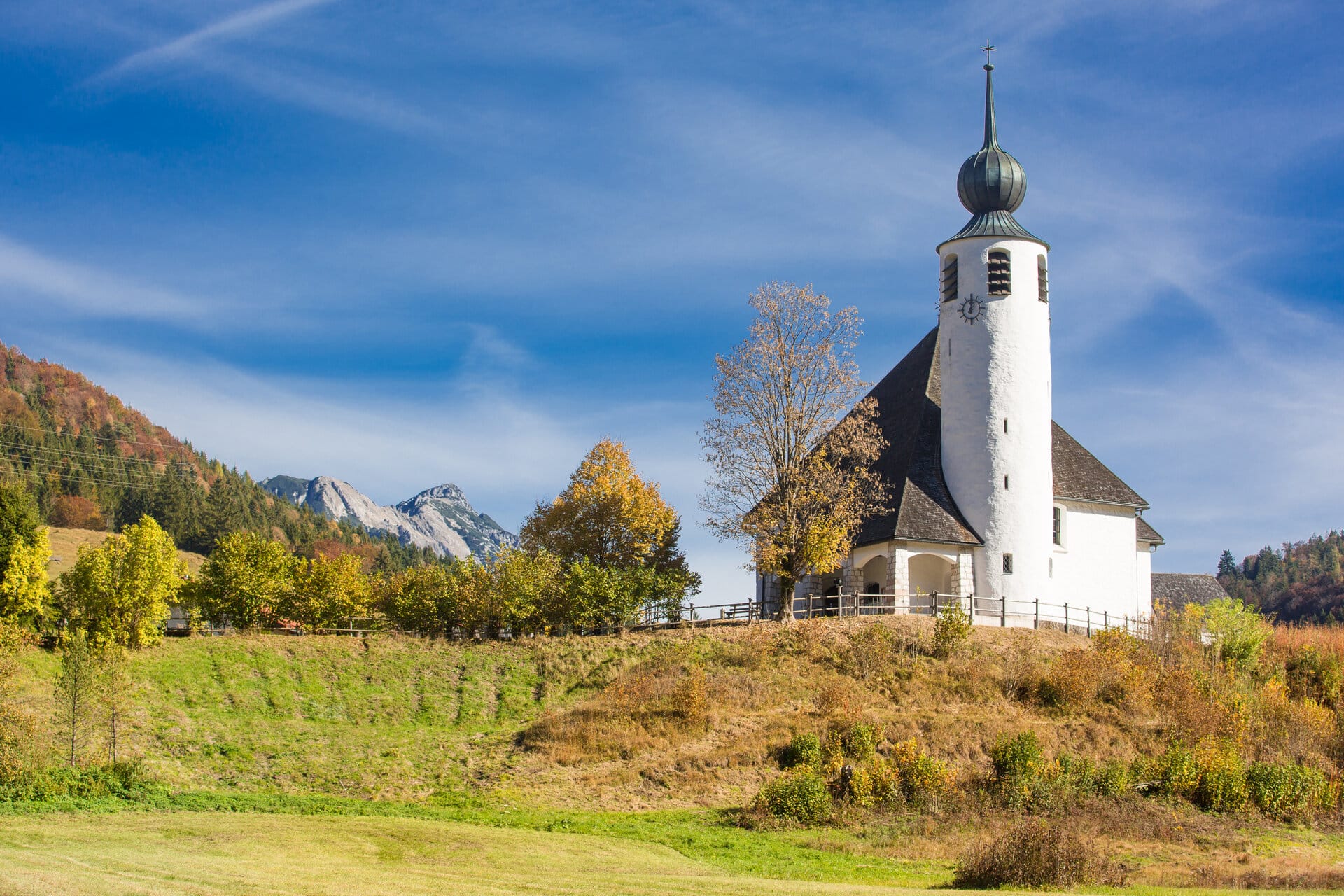 Kapelle an der Deutschen Alpenstraße im Herbst bei Sonnenschein mit Bergen im Hintergrund