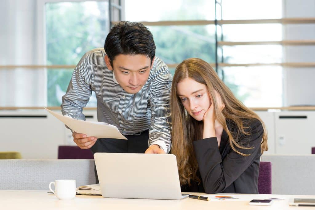 Junge Frau am Schreibtisch wird von einem Kollegen in einen neuen Job eingewiesen