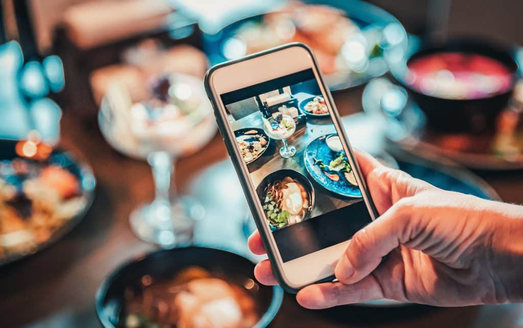 Foodfoto im Restaurant Hand mit Mobiltelefon nimmt verschiedene Teller mit Speisen auf einem Tisch auf