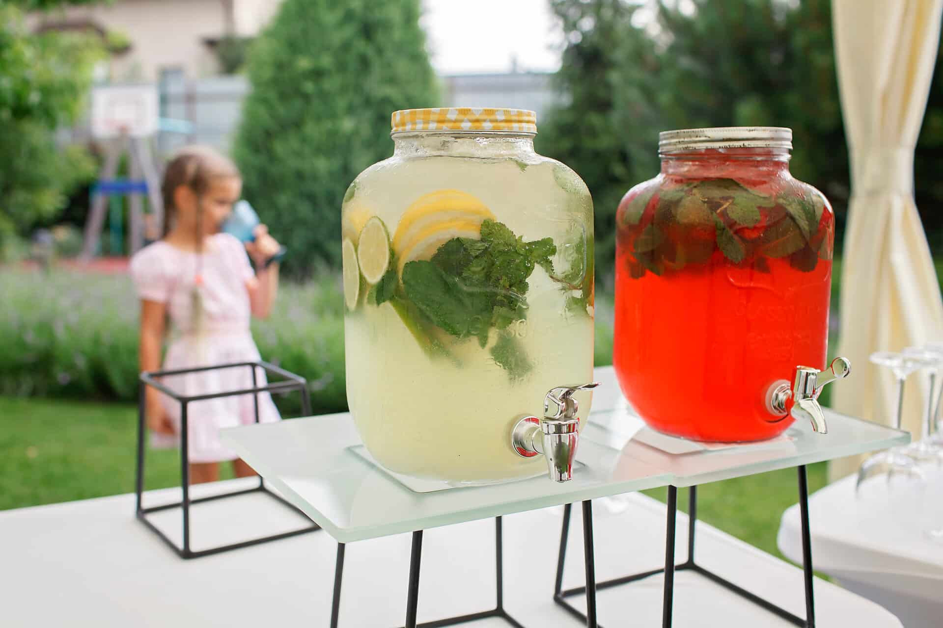 Girl holding a glass of colorful natural fruits lemonade during backyard barbeque party at summer, elegant decoration, luxury catering, drink and buffet standing reception, festive celebration