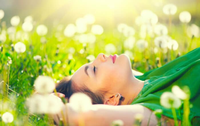 Junge Frau liegt im Gras mit Pusteblumen und schließt entspannt die Augen Nahaufnahme des Kopfes