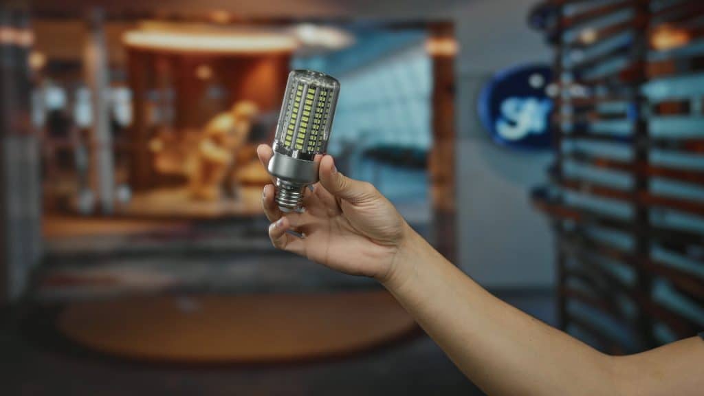 Hand holding led light bulb in modern hotel lobby, showcasing energy-efficient design and indoor lighting solutions in a contemporary setting.