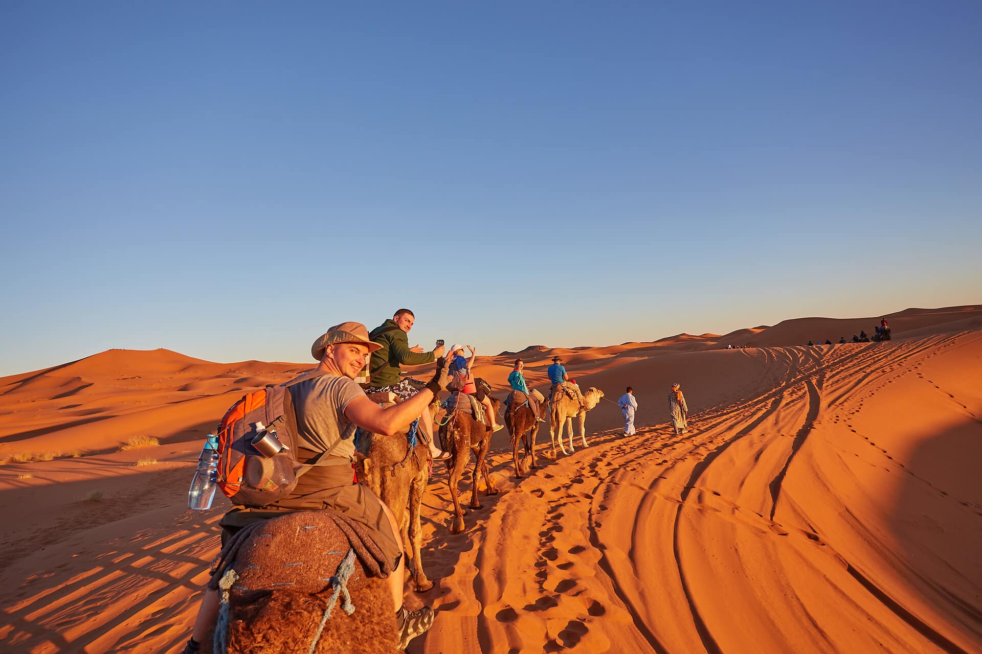 A group of cheerful tourists embarks on a camel safari, exploring the enchanting Sahara Desert in Morocco