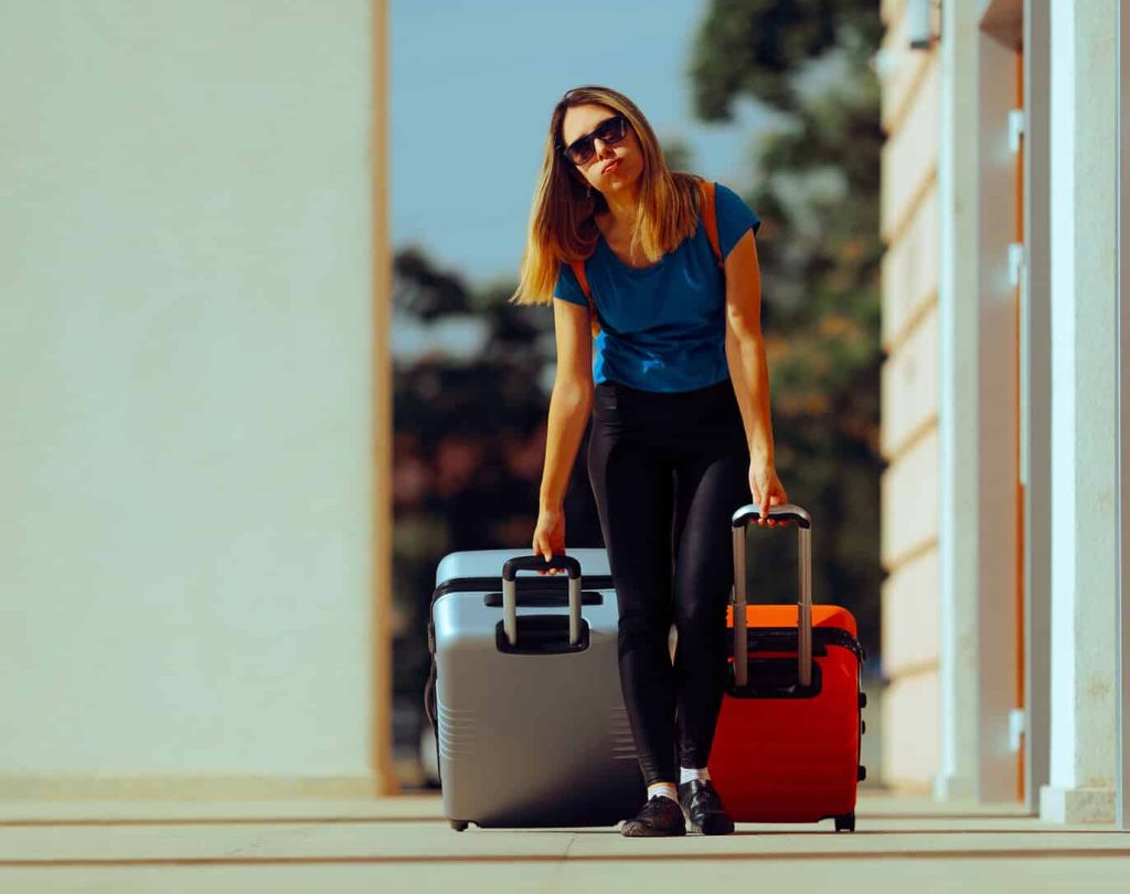 Frau mit Sonnenbrille zieht 2 schwere Koffer hinter sich her.